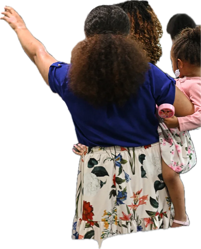 A mother worshipping with one hand raised while carrying her young daughter.